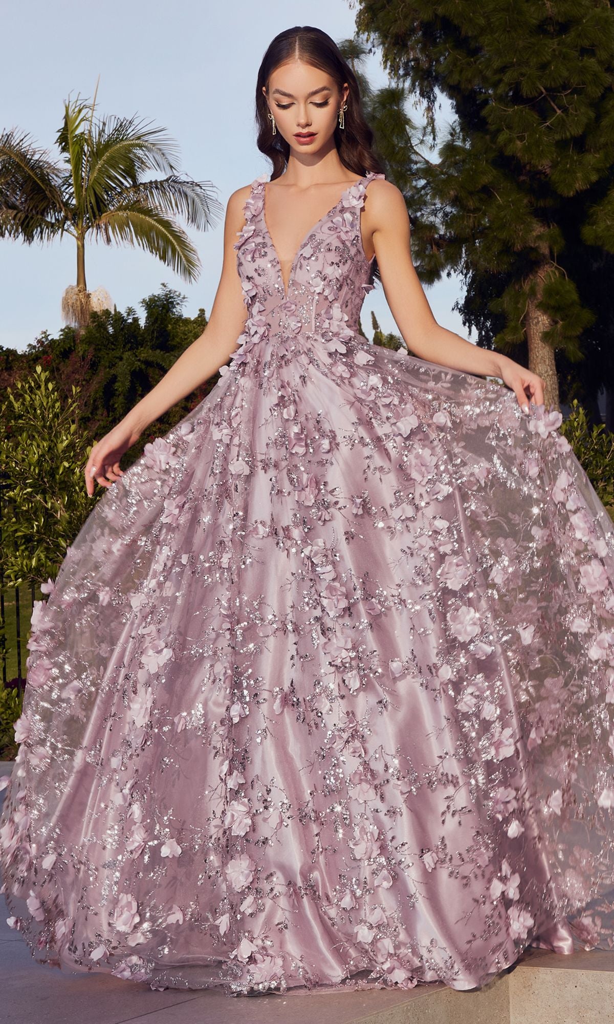 A woman stands outdoors, holding the sides of her Long Glitter-Floral A-Line Prom Ball Gown J838, a light purple evening dress with floral details and a deep V-neckline, surrounded by trees and greenery.